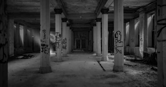 A black and white photo of a dark room with large columns forming a hallway down the center.